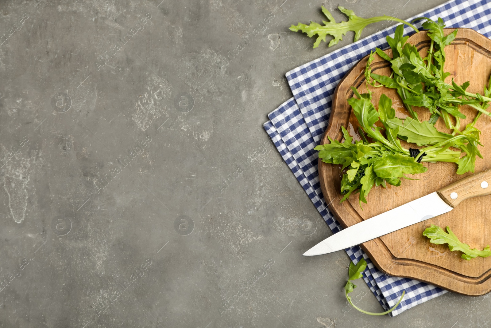 Photo of Fresh arugula, cutting board and knife on grey table, flat lay. Space for text