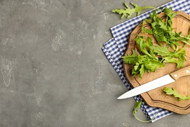 Photo of Fresh arugula, cutting board and knife on grey table, flat lay. Space for text