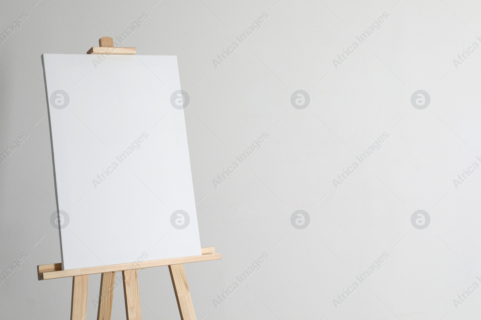 Photo of Wooden easel with blank canvas on light background. Space for text