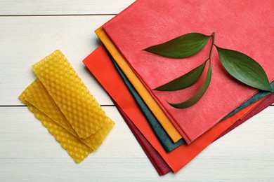 Photo of Colorful beeswax food wraps and fresh leaves on white wooden table, flat lay