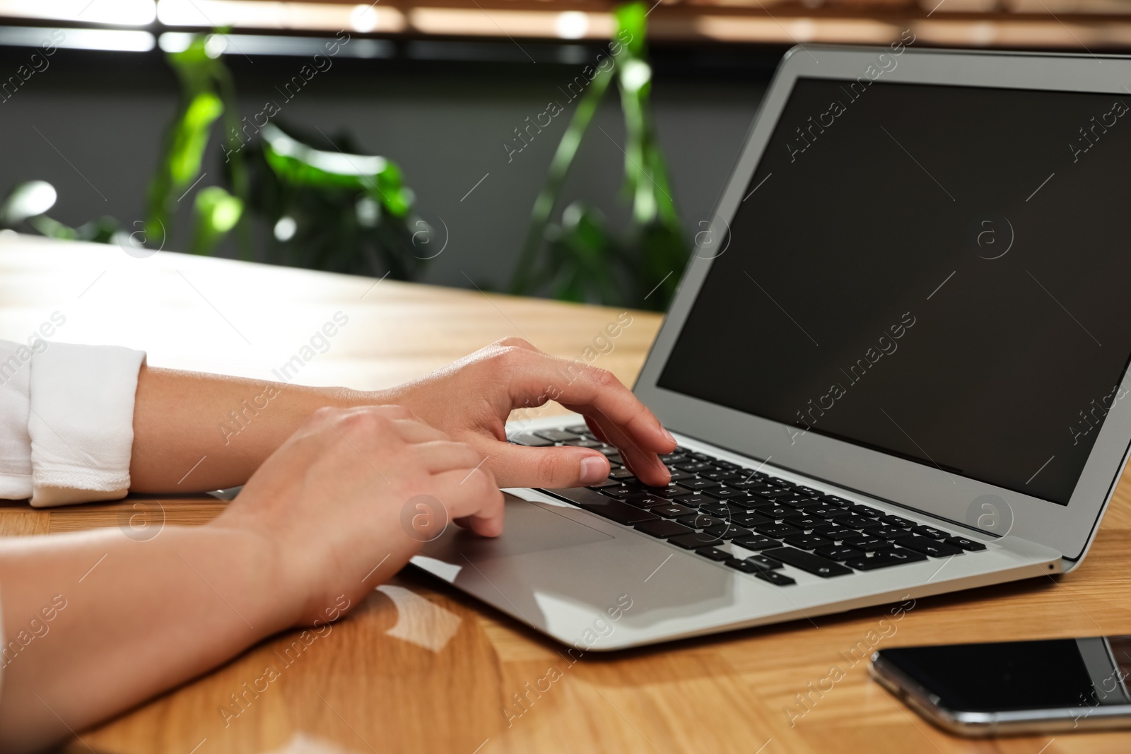 Photo of Young woman using laptop for search at wooden table in room, closeup