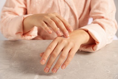 Photo of Woman applying cosmetic cream onto hand at grey table, closeup
