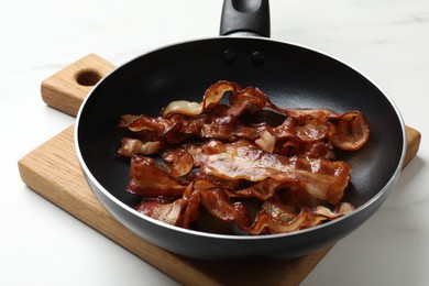 Photo of Delicious bacon slices in frying pan on white table, closeup