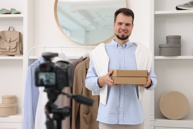 Photo of Smiling fashion blogger with cardboard boxes recording video at home