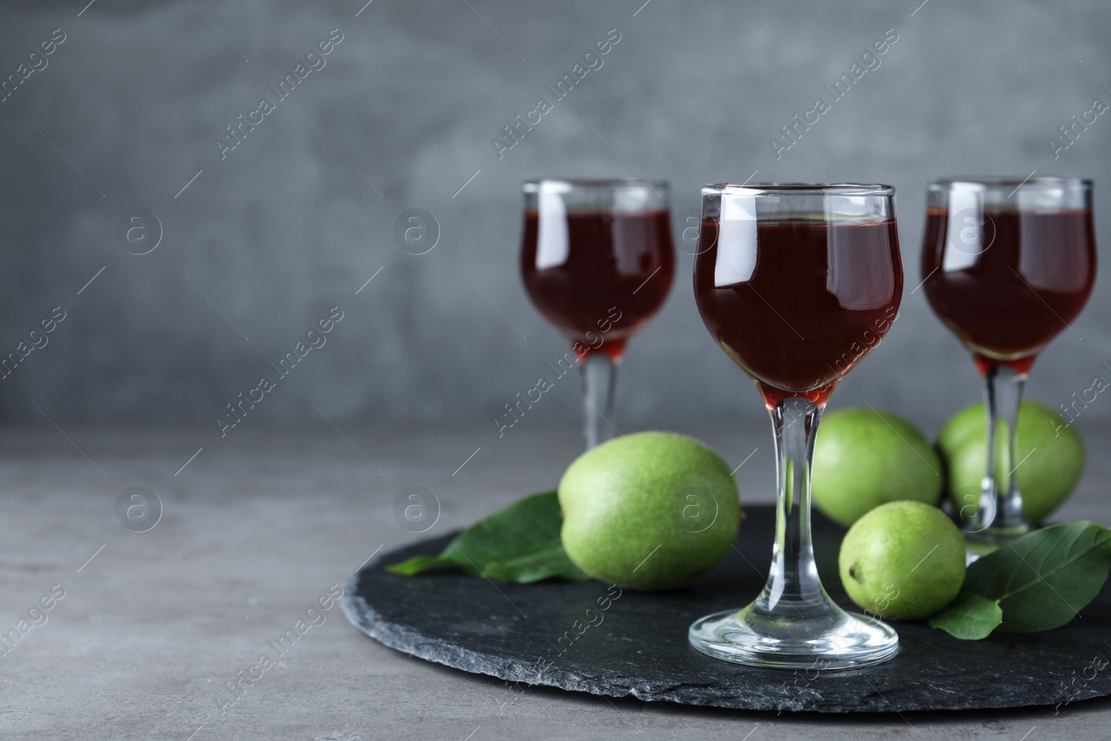 Photo of Delicious liqueur and green walnuts on grey table. Space for text