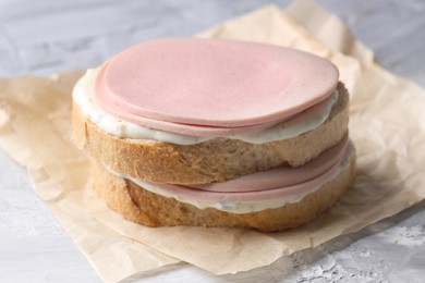 Delicious sandwich with boiled sausage and sauce on grey textured table, closeup