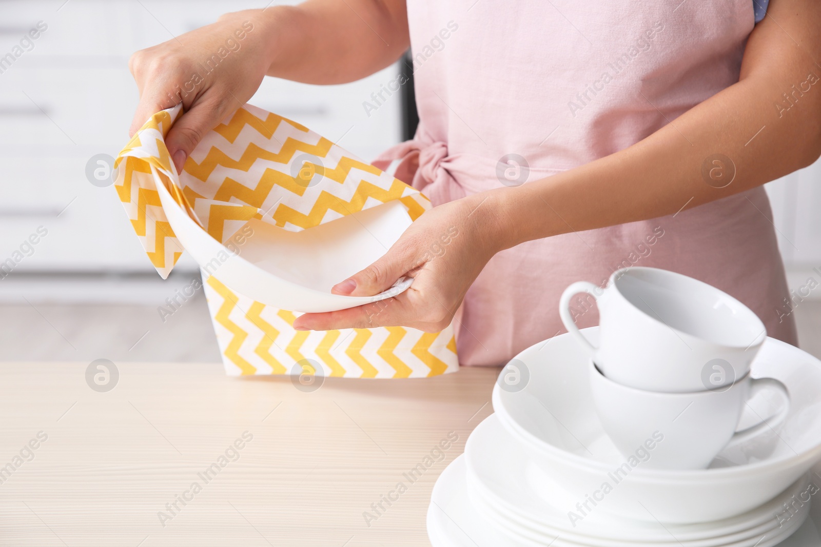 Photo of Woman wiping clean dish at table in kitchen, closeup