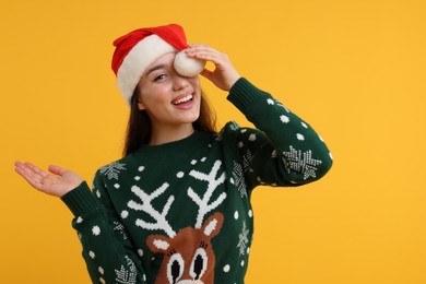 Photo of Happy young woman in Christmas sweater and Santa hat on orange background. Space for text