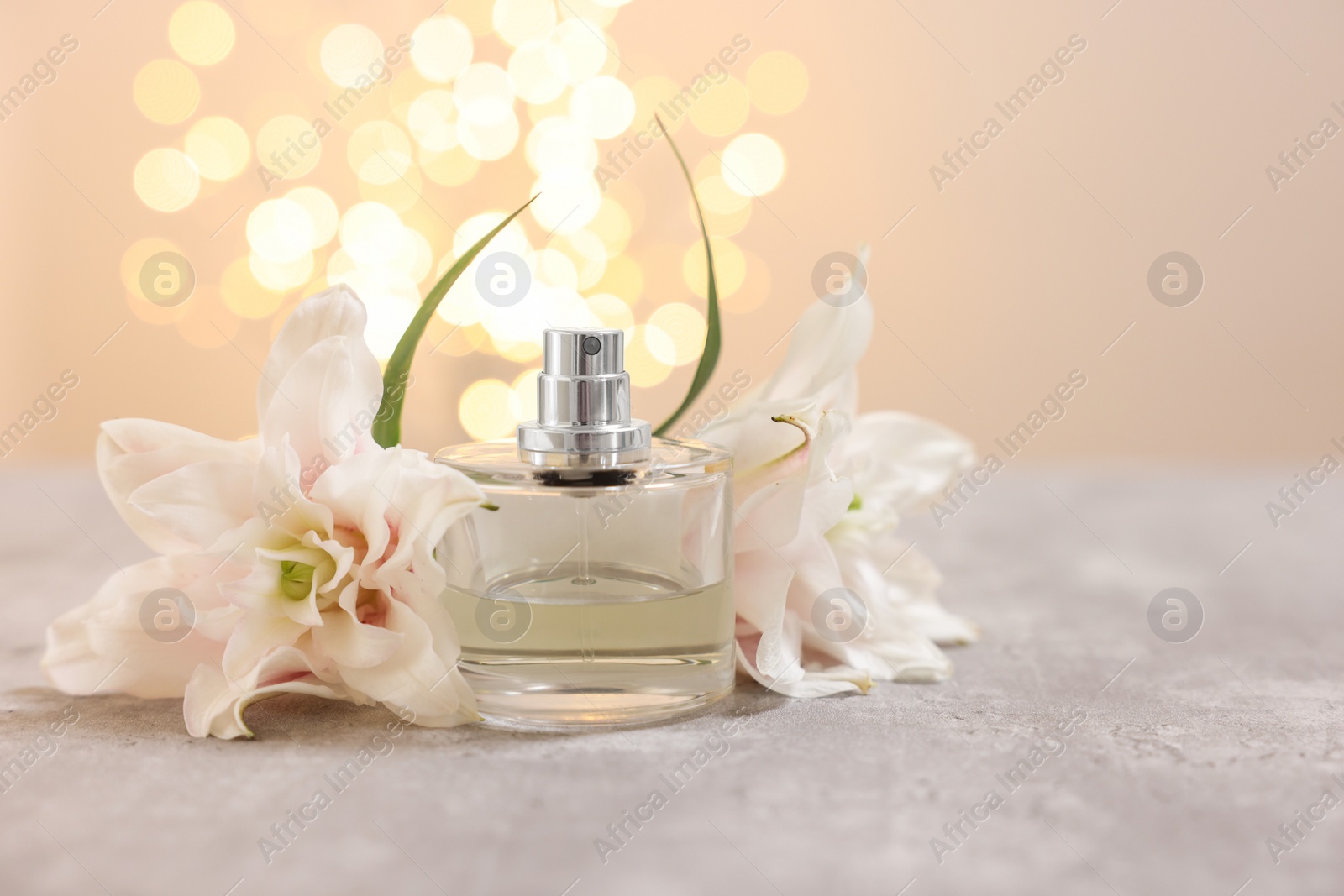 Photo of Bottle of perfume and beautiful lily flowers on table against beige background with blurred lights, space for text