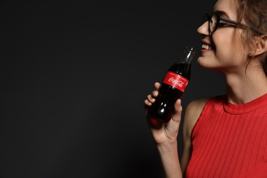 MYKOLAIV, UKRAINE - NOVEMBER 28, 2018: Young woman with bottle of Coca-Cola on dark background, space for text