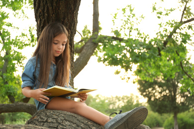 Photo of Cute little girl reading book on tree in park