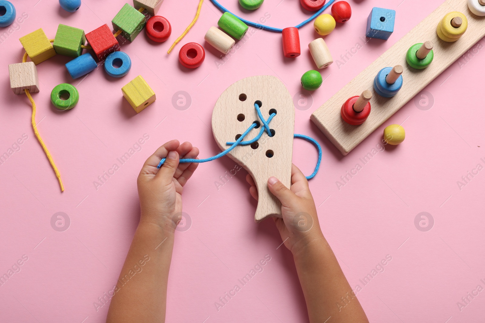 Photo of Motor skills development. Little child playing with wooden lacing toy at pink table, top view