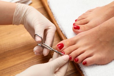 Pedicurist cutting client`s toenails with scissors in beauty salon, closeup