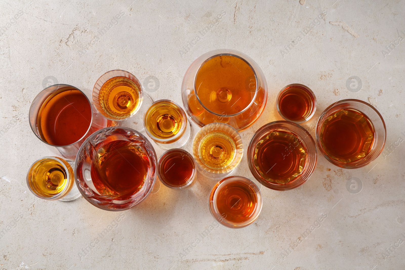 Photo of Different delicious liqueurs in glasses on light grey table, flat lay