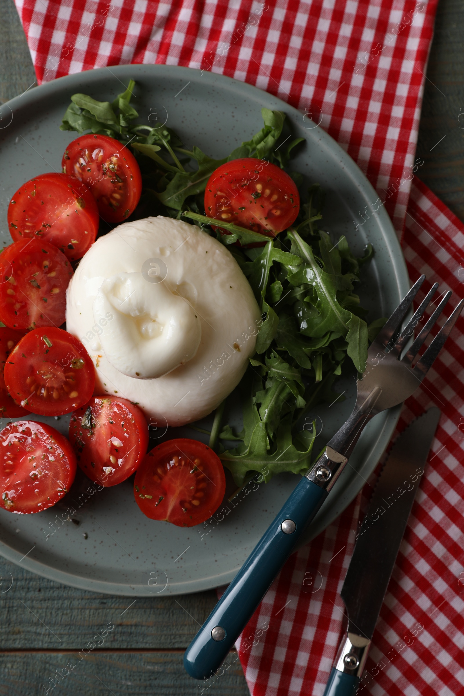 Photo of Delicious burrata cheese with tomatoes and arugula served on grey wooden table, flat lay