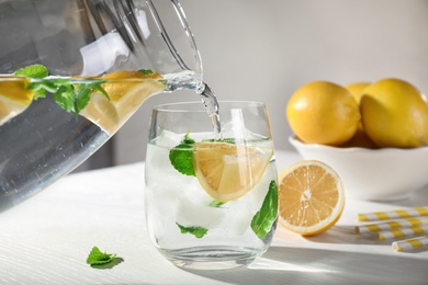 Photo of Pouring of refreshing lemonade into glass on white table