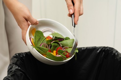 Woman throwing vegetable salad into bin indoors, closeup