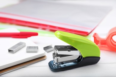 Photo of New bright stapler with stationery on white wooden table