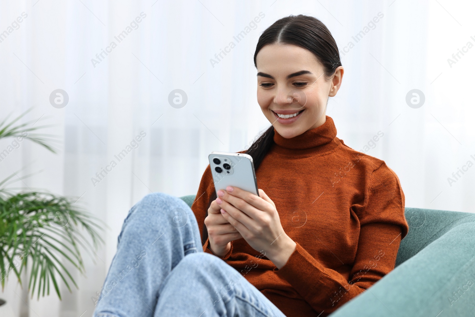 Photo of Happy young woman using smartphone on sofa at home