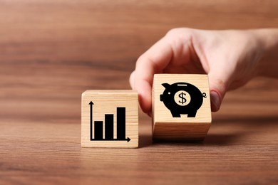 Woman putting cube with piggy bank and dollar sign near other one with chart on wooden table, closeup