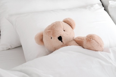 Photo of Cute teddy bear lying in bed indoors