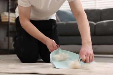 Man with brush and pan removing pet hair from carpet at home, closeup