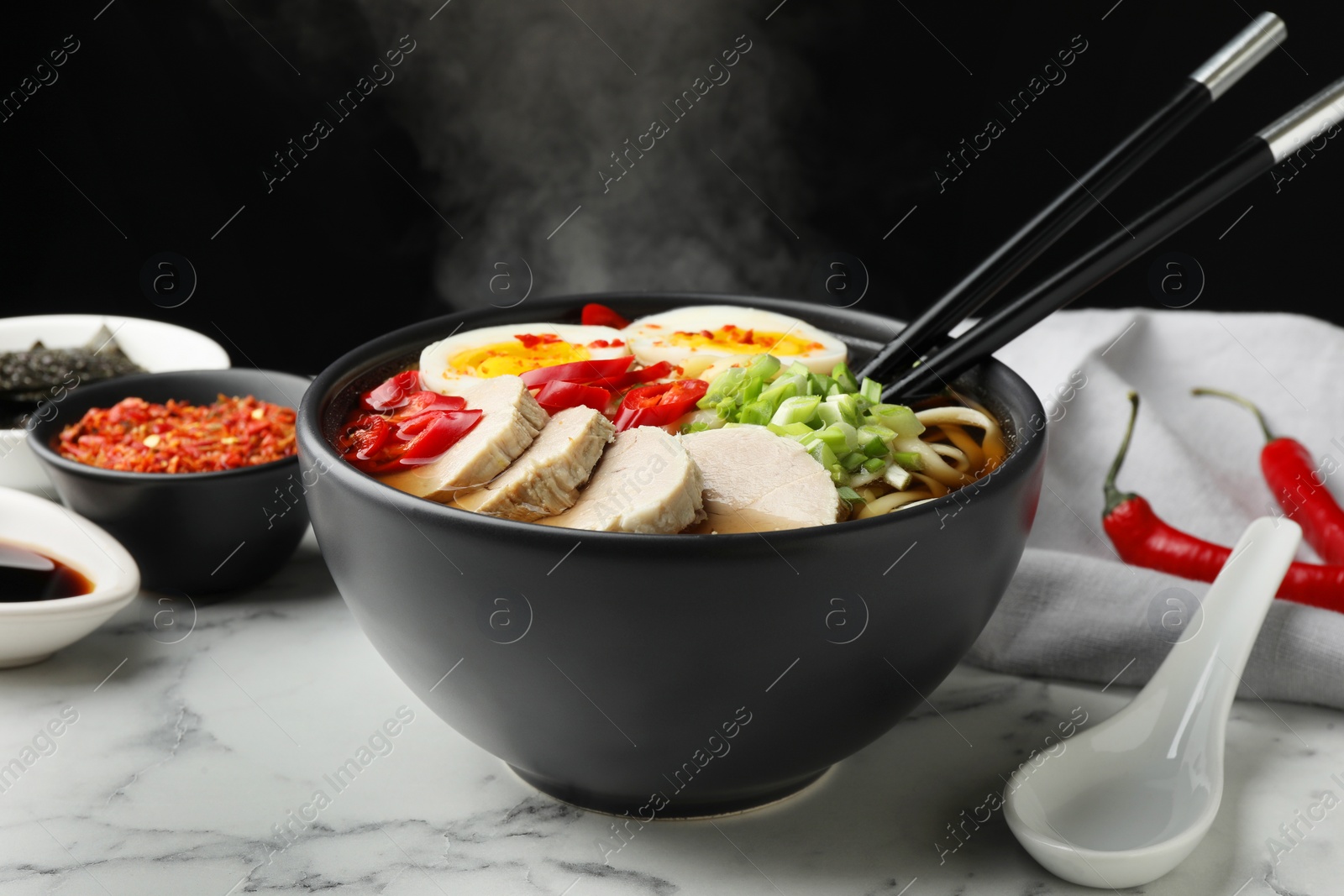 Photo of Delicious ramen in bowl on white marble table against black background, closeup. Noodle soup