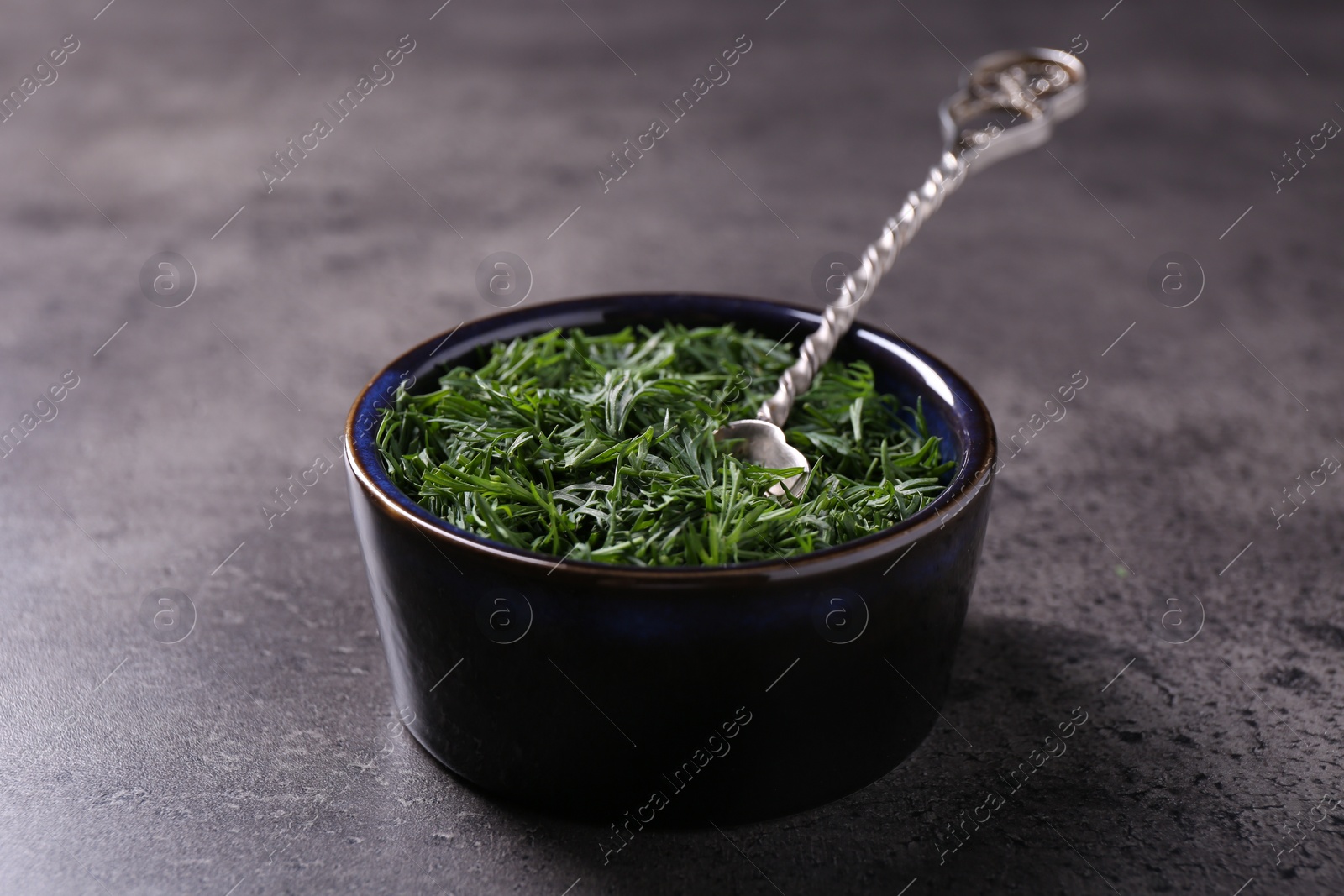 Photo of Fresh cut dill in bowl and spoon on grey textured table, closeup