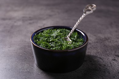 Fresh cut dill in bowl and spoon on grey textured table, closeup