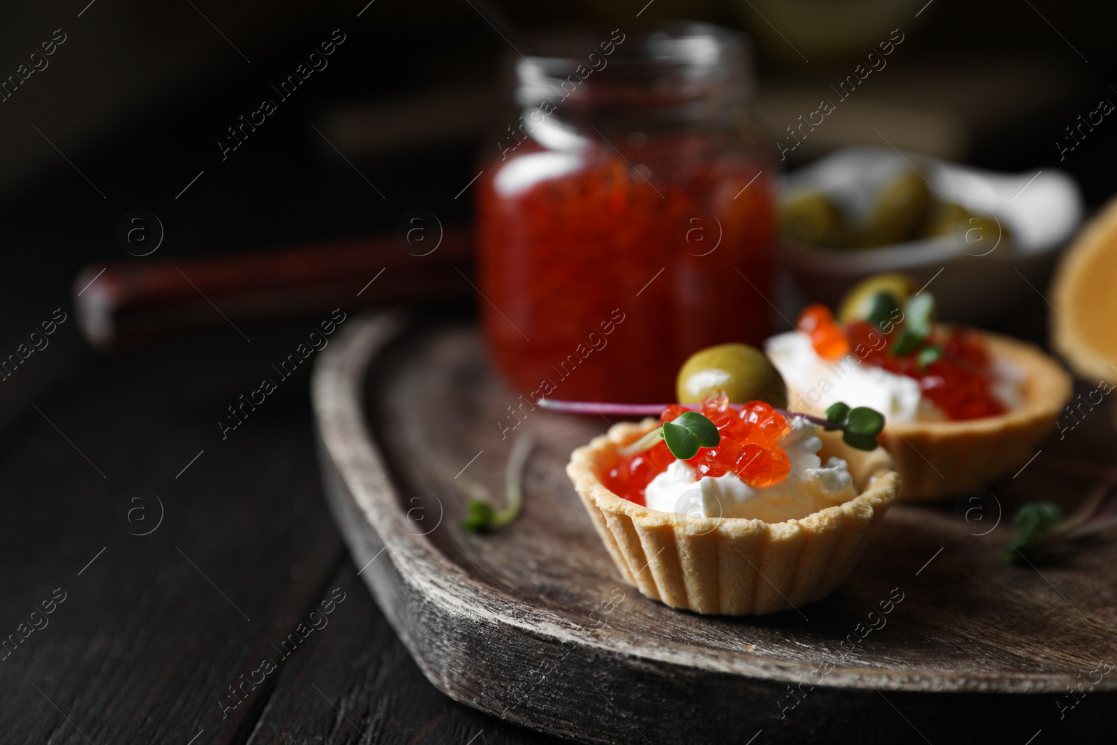 Photo of Delicious tartlets with red caviar and cream cheese served on wooden table, closeup