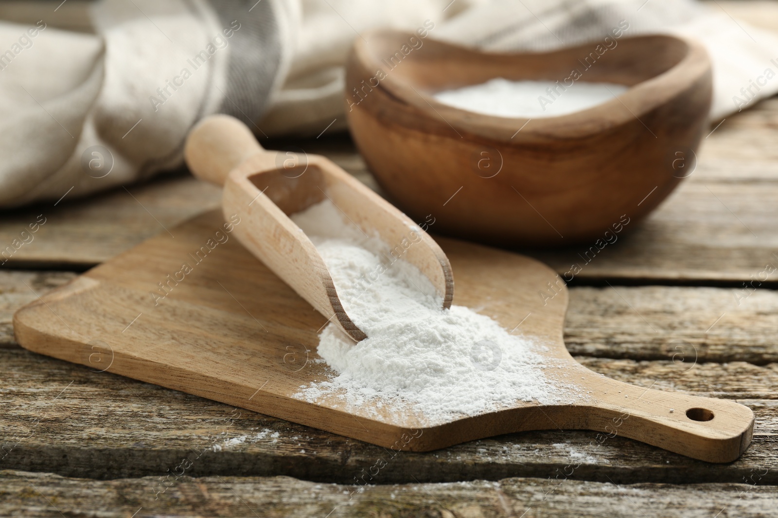 Photo of Baking powder in scoop and bowl on wooden table, closeup