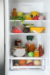 Photo of Open refrigerator with many different products packed in beeswax food wraps