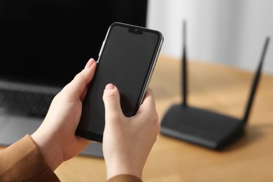 Photo of Woman with smartphone connecting to internet via Wi-Fi router at table indoors, closeup