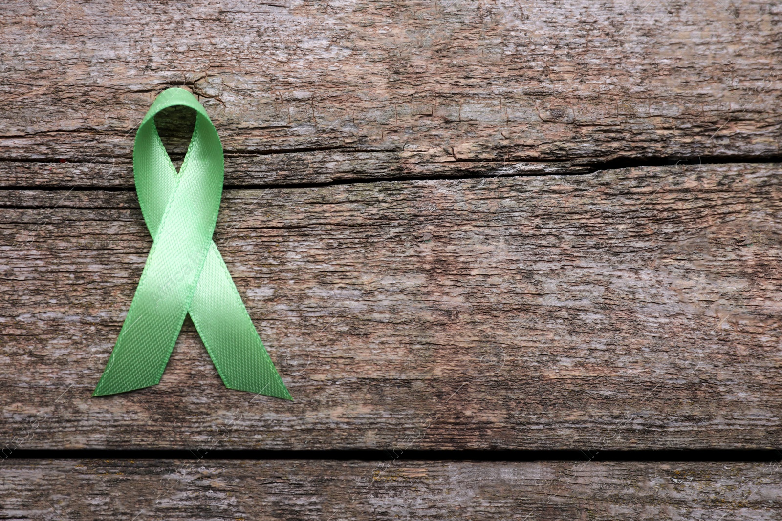 Photo of World Mental Health Day. Green ribbon on wooden background, top view with space for text