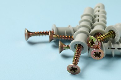 Photo of Many metal screws with dowels on light blue background, closeup. Space for text