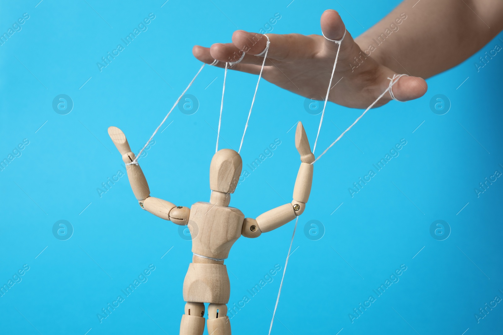 Photo of Woman pulling strings of puppet on light blue background, closeup