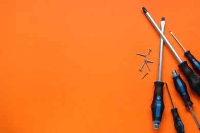 Photo of Set of screwdrivers and screws on orange background, flat lay. Space for text