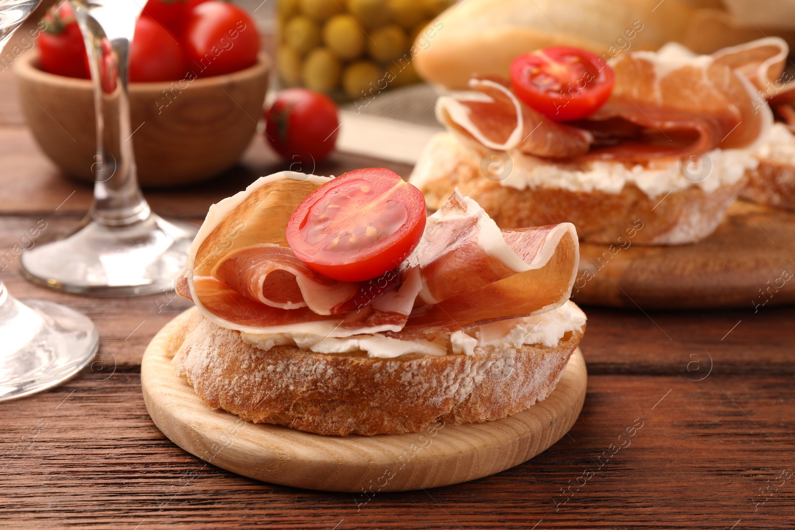 Photo of Tasty sandwich with cured ham, tomato and cream cheese on wooden table, closeup