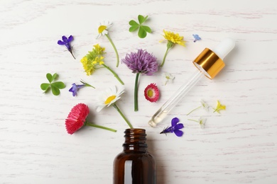 Photo of Bottle of essential oil and different flowers on white wooden background, flat lay