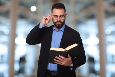 Confident lawyer in glasses reading book on blurred background