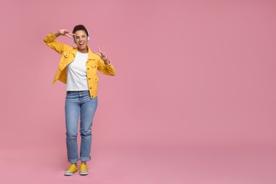 Happy young woman in headphones dancing on pink background. Space for text