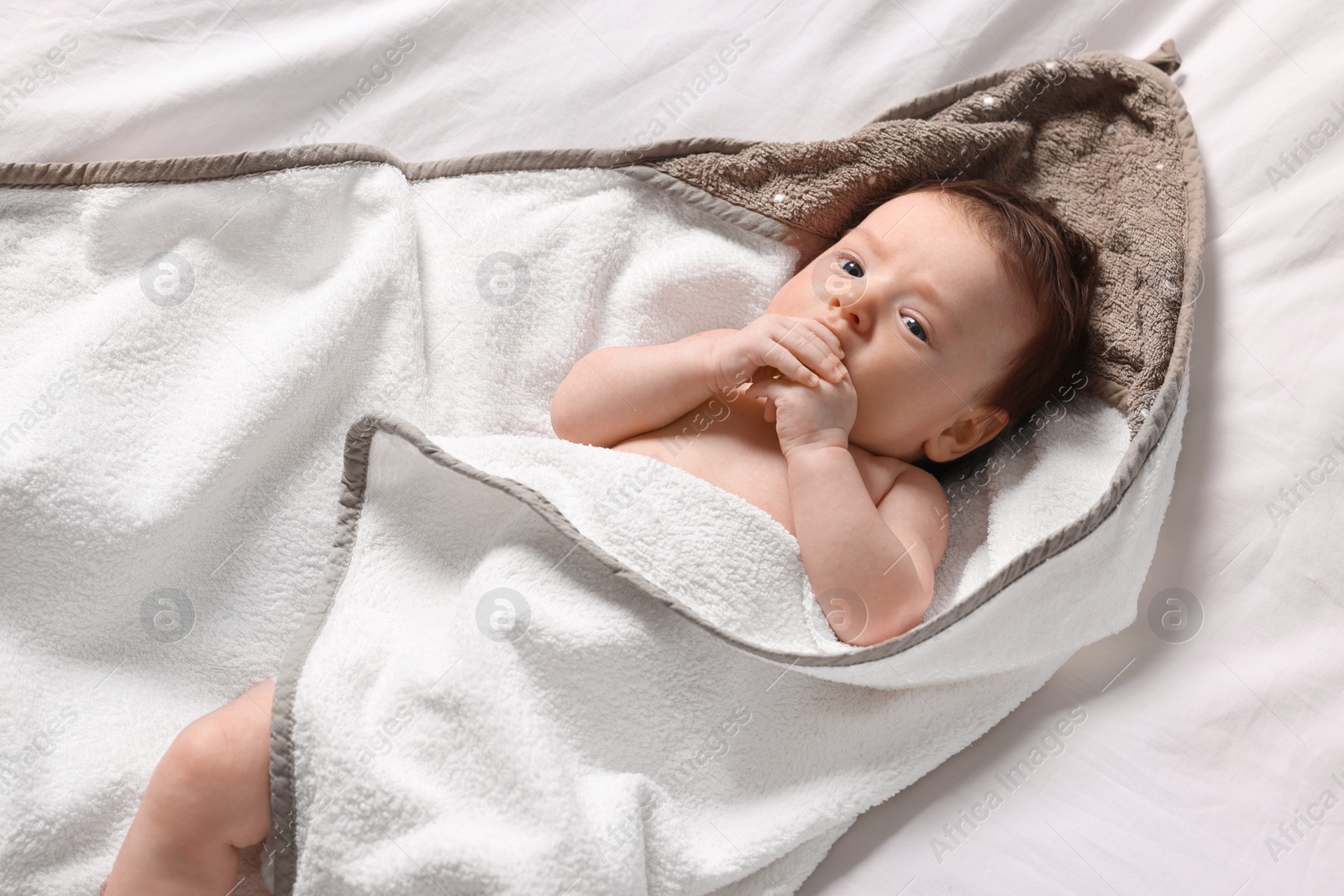 Photo of Cute little baby in hooded towel after bathing on bed, top view