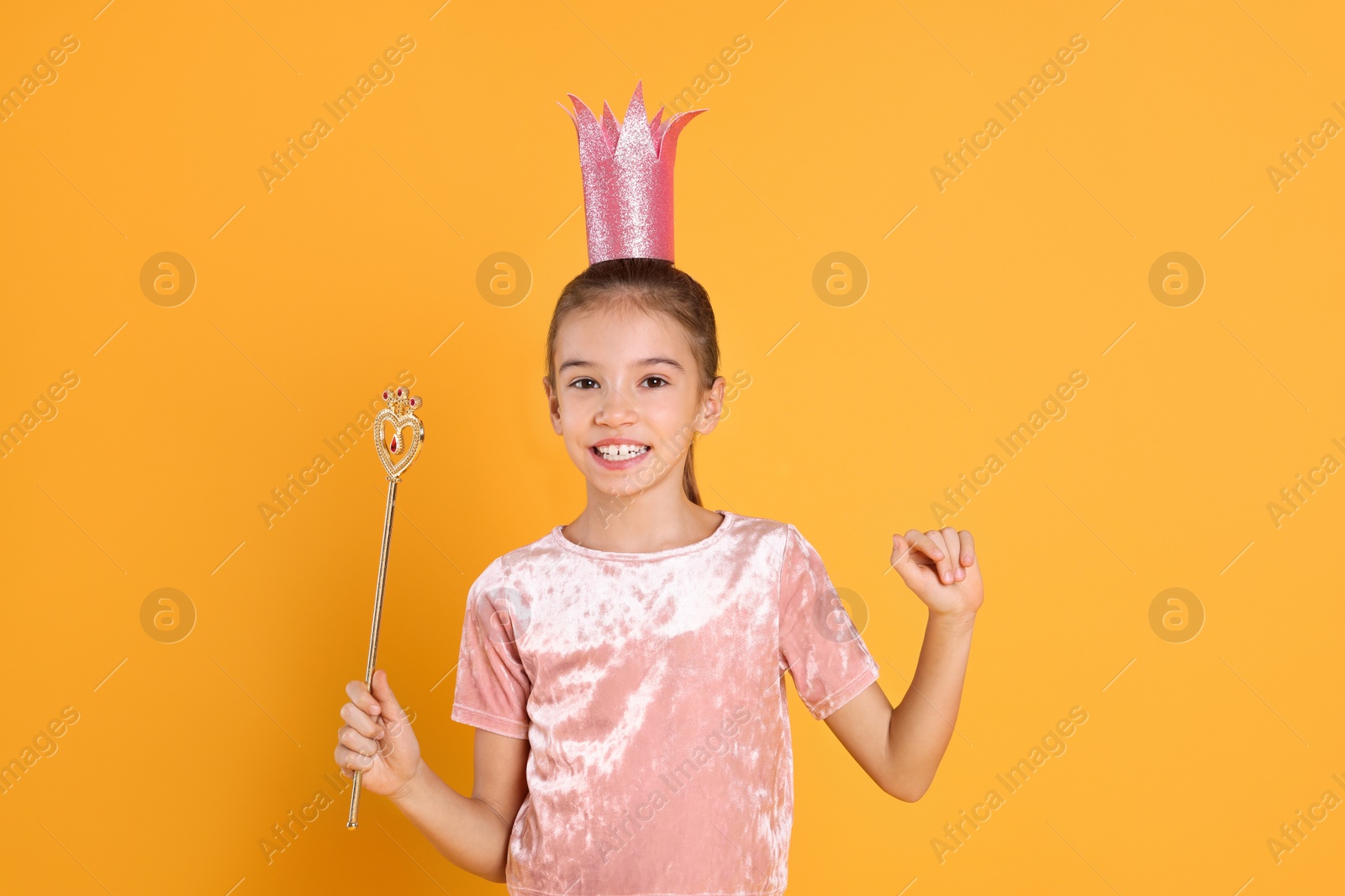 Photo of Cute girl in pink crown with magic wand on yellow background. Little princess