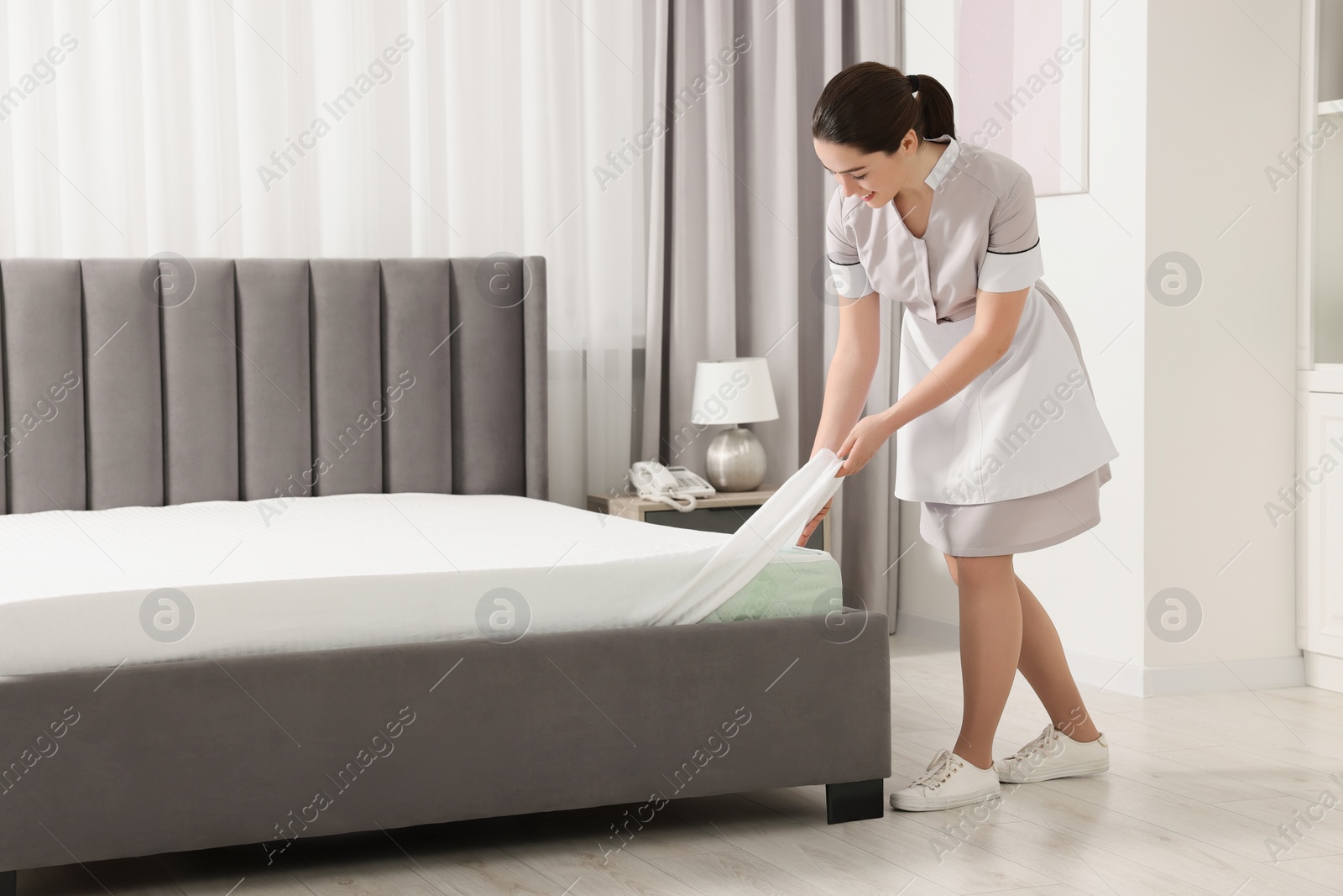 Photo of Young maid making bed in hotel room. Space for text