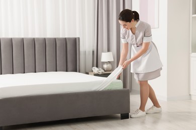 Young maid making bed in hotel room. Space for text