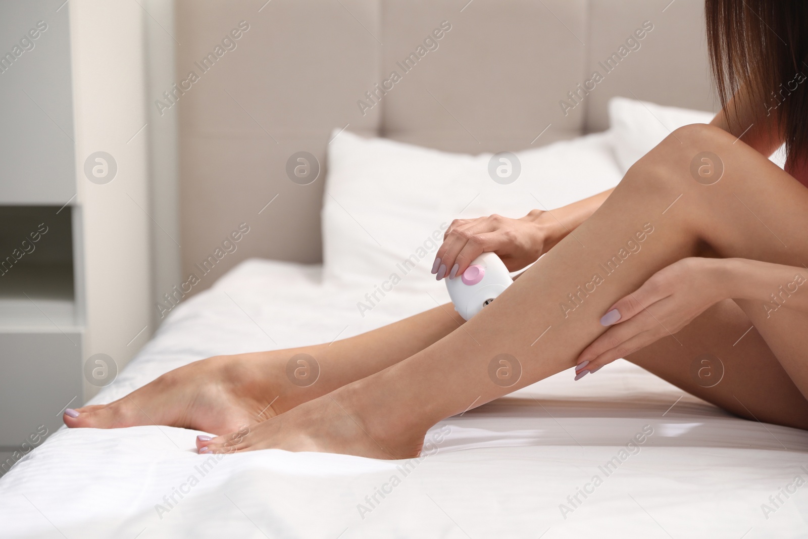 Photo of Young woman epilating her legs in bedroom, closeup