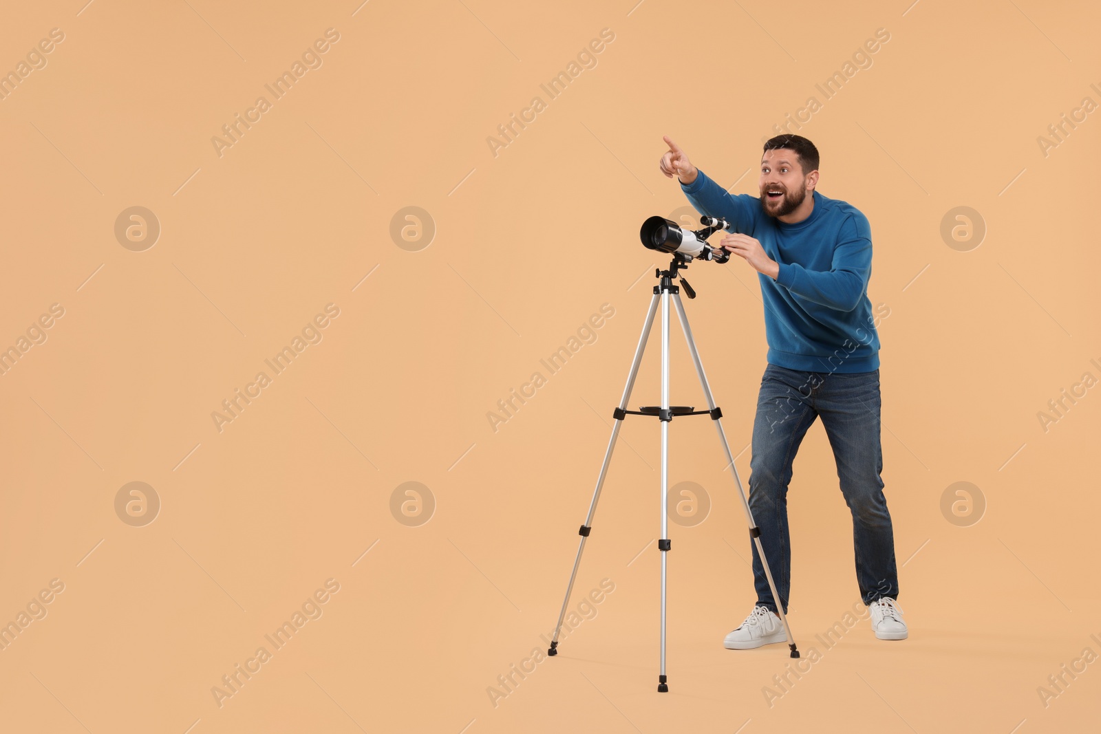 Photo of Happy astronomer with telescope pointing at something on beige background. Space for text