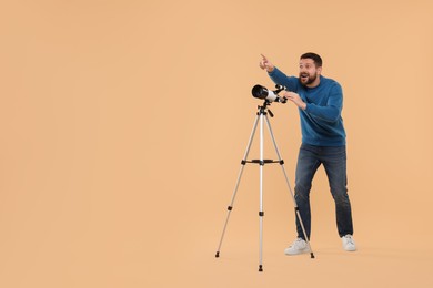 Happy astronomer with telescope pointing at something on beige background. Space for text