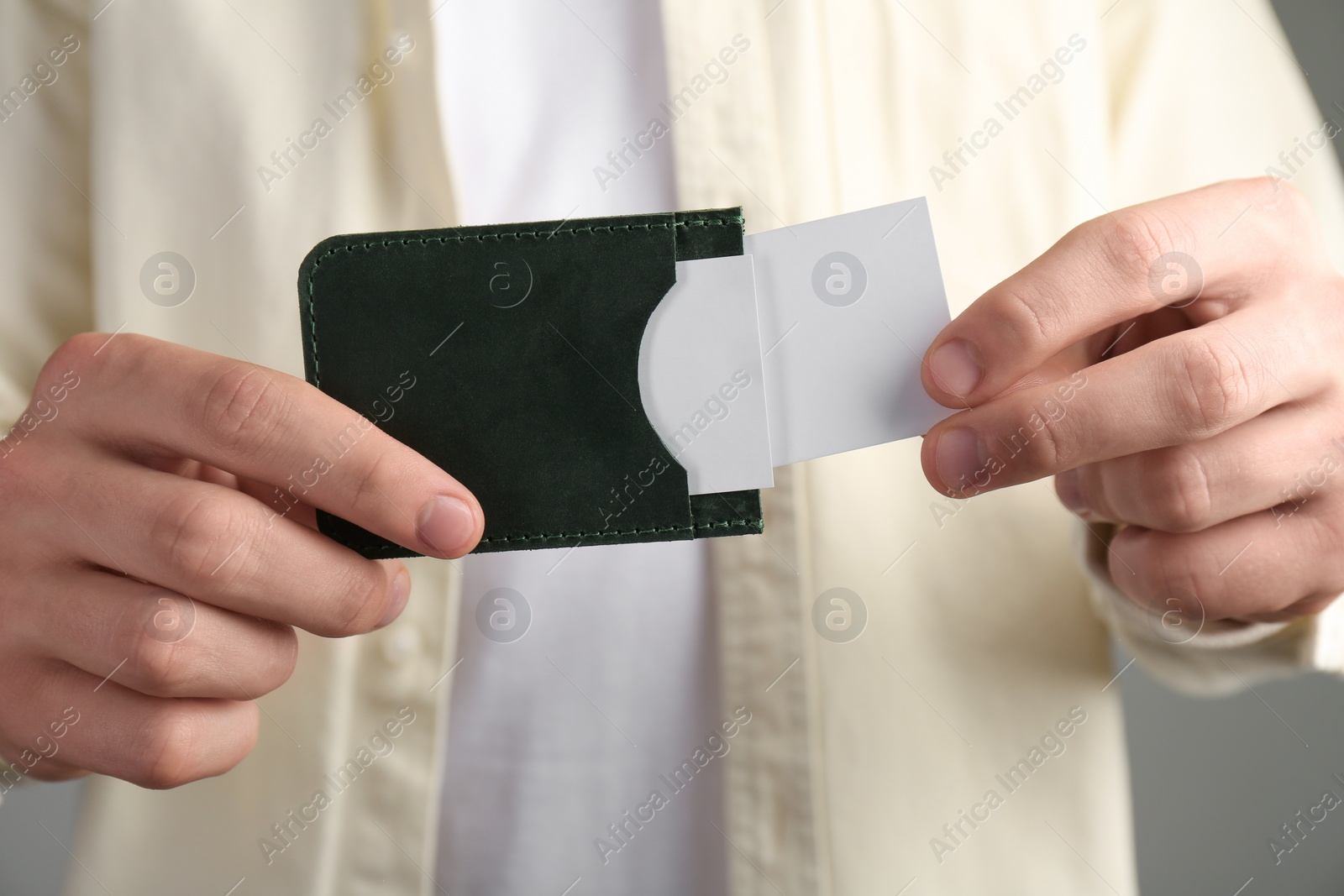 Photo of Man holding leather business card holder with cards on grey background, closeup