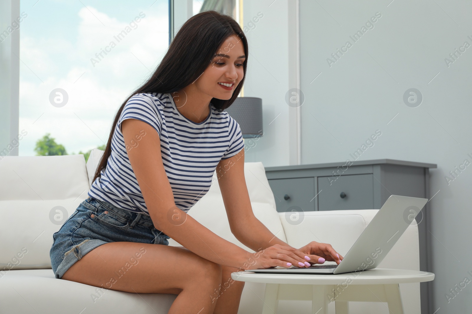 Photo of Young woman using laptop on sofa at home. Internet shopping